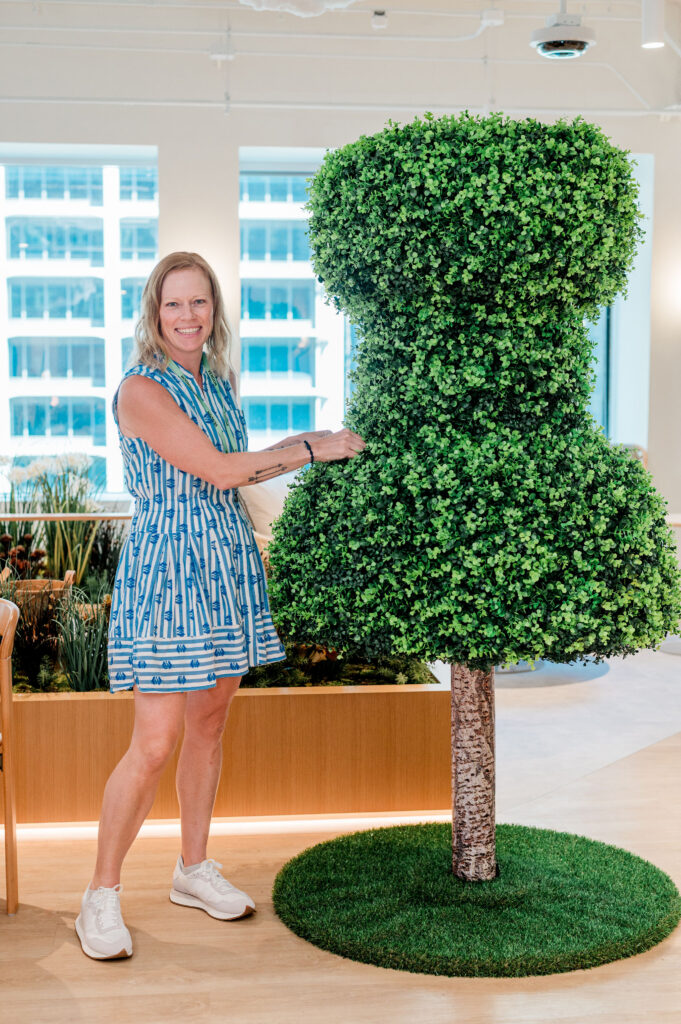 Custom pin-shaped green topiary centerpiece amidst immersive garden event decor