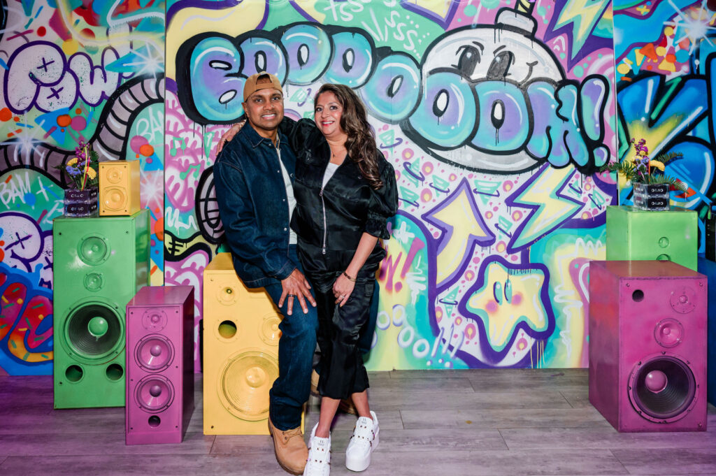 A couple leaning up against brightly painted speakers that are a prop. A custom graffiti backdrop is in the background