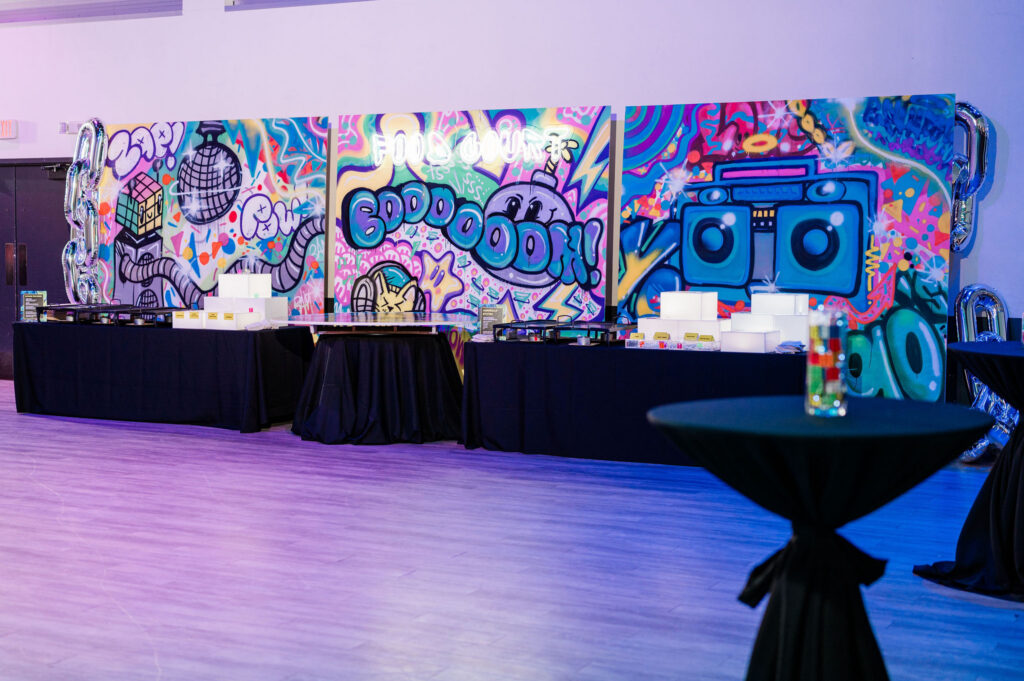 3 backdrop walls next to each together that have been custom graffitied. Tables for food are in front of them.