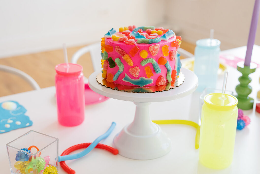 A bright tablescape with colorful cups, plates and candles and a close up of a gummy pink cake