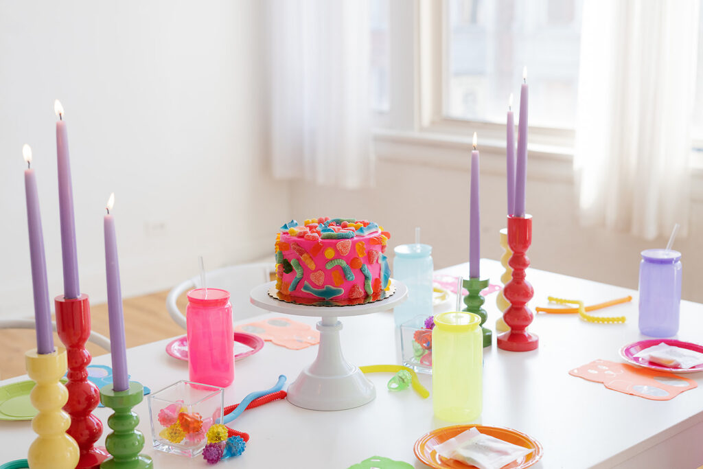 A bright tablescape with colorful cups, plates and candles and a gummy pink cake