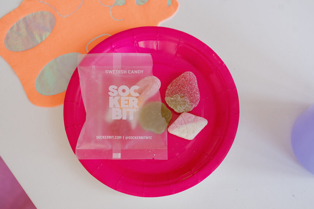 A close up photo of the place setting of a orange gummy bear napkin and pink plate with a small package of sockerbit gummies on the plate