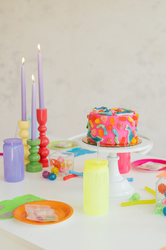 A bright tablescape with colorful cups, plates and candles and a gummy pink cake