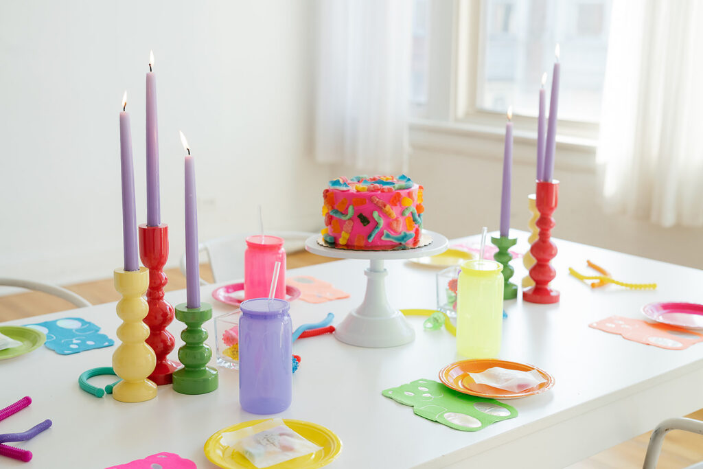 A bright tablescape with colorful cups, plates and candles and a gummy pink cake