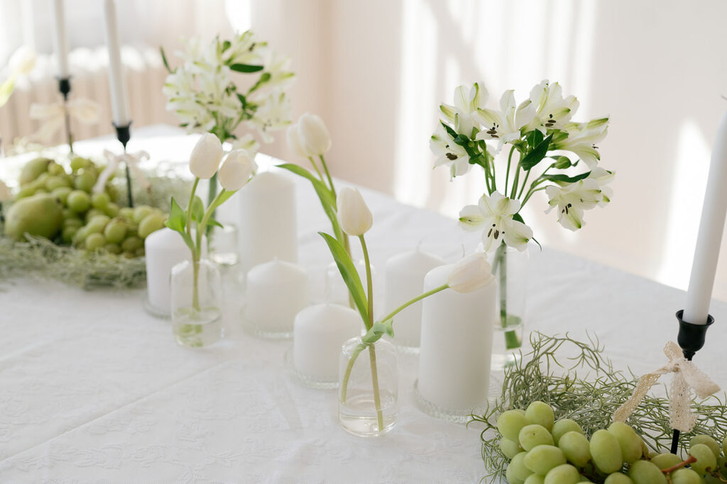 A food and lace themed tablescape with black and white candlesticks, white flowers grapes and pears