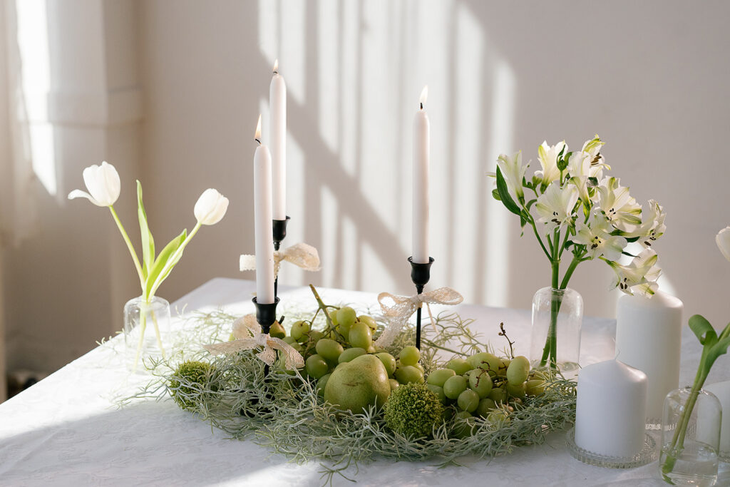 A food and lace themed tablescape with black and white candlesticks, white flowers grapes and pears