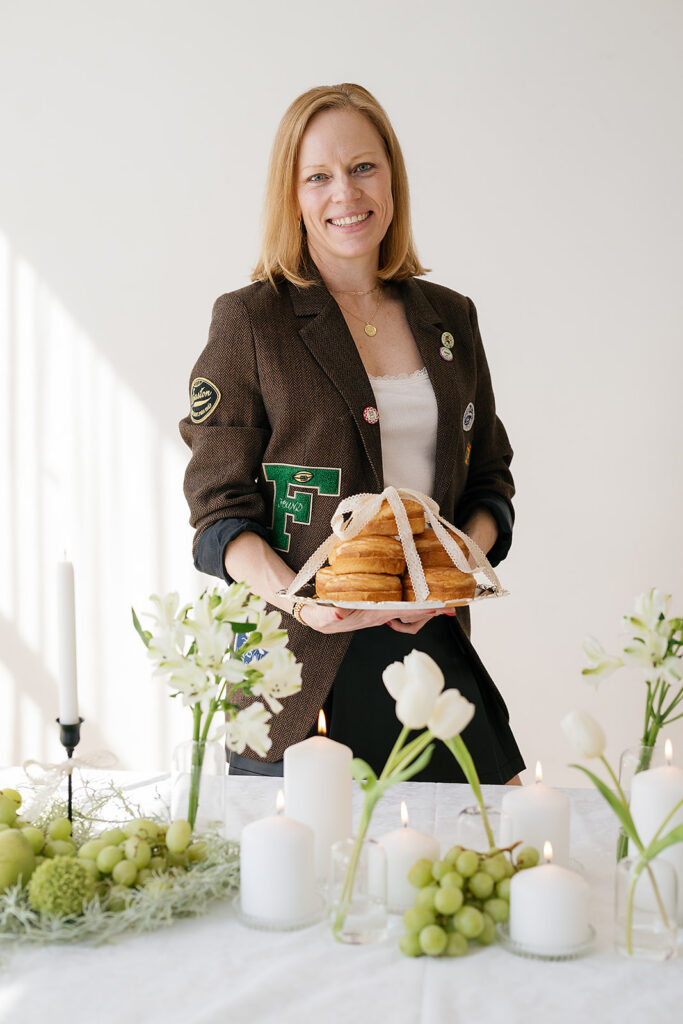 Jessie the founder of WE EVENTS leaning up against a food holding a plate with bread and a lace ribbon around the plate. The tablescape is gren and white and black. 