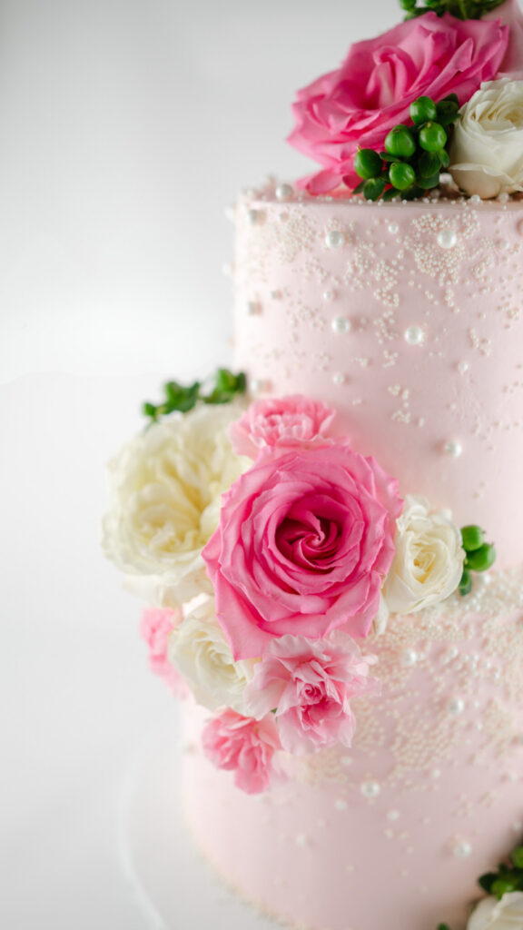 A pin 2 tier cake with bright pink and white flowers and edible pearls