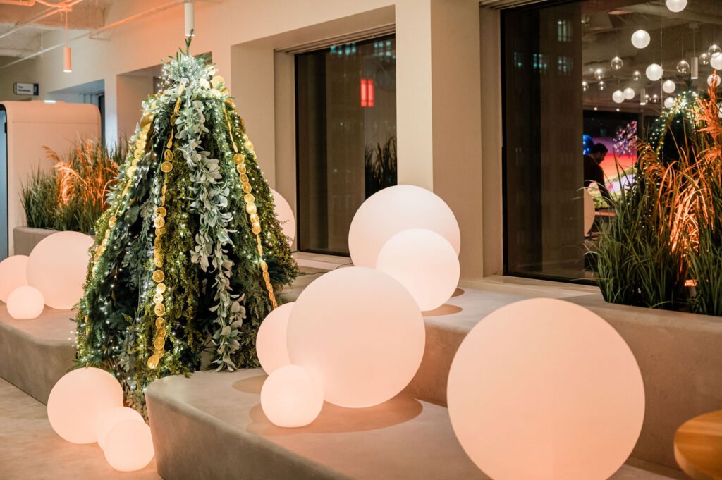 A tree that is adorned with lots of different greenery and dried oranges. Large soft white orbs are on the couches next to it.