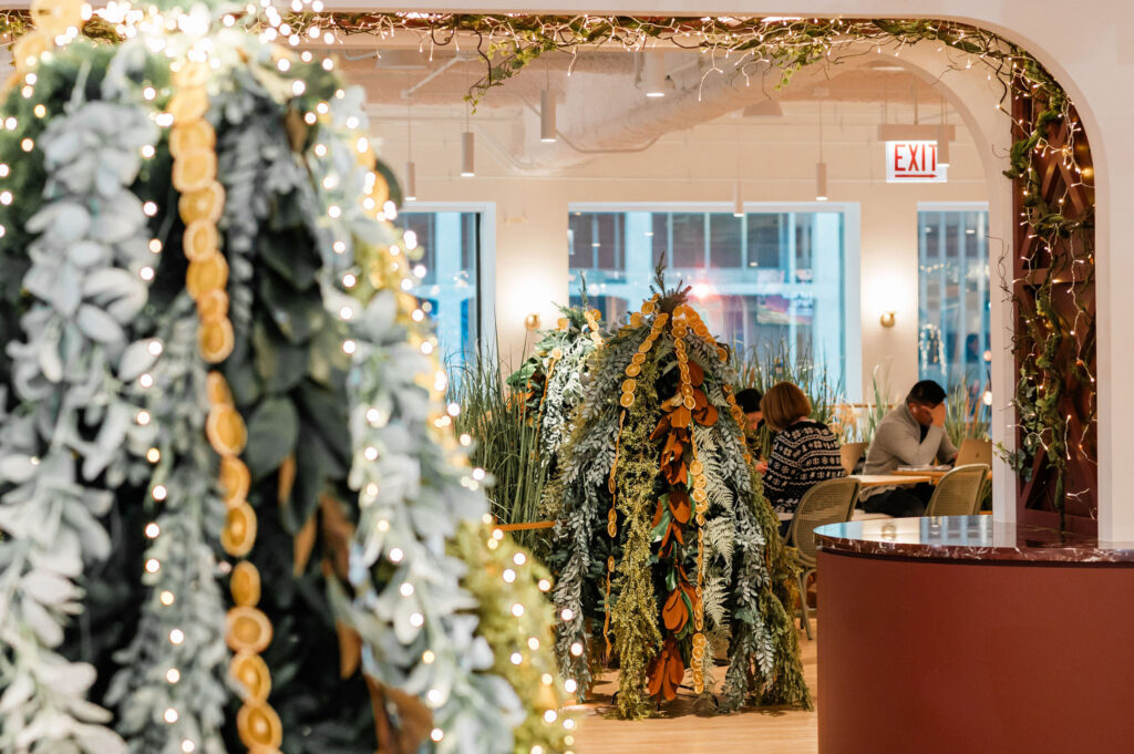 There are 2 heavily decorated evergreen tree. The trees are adorned with lots of different greenery and dried oranges. 