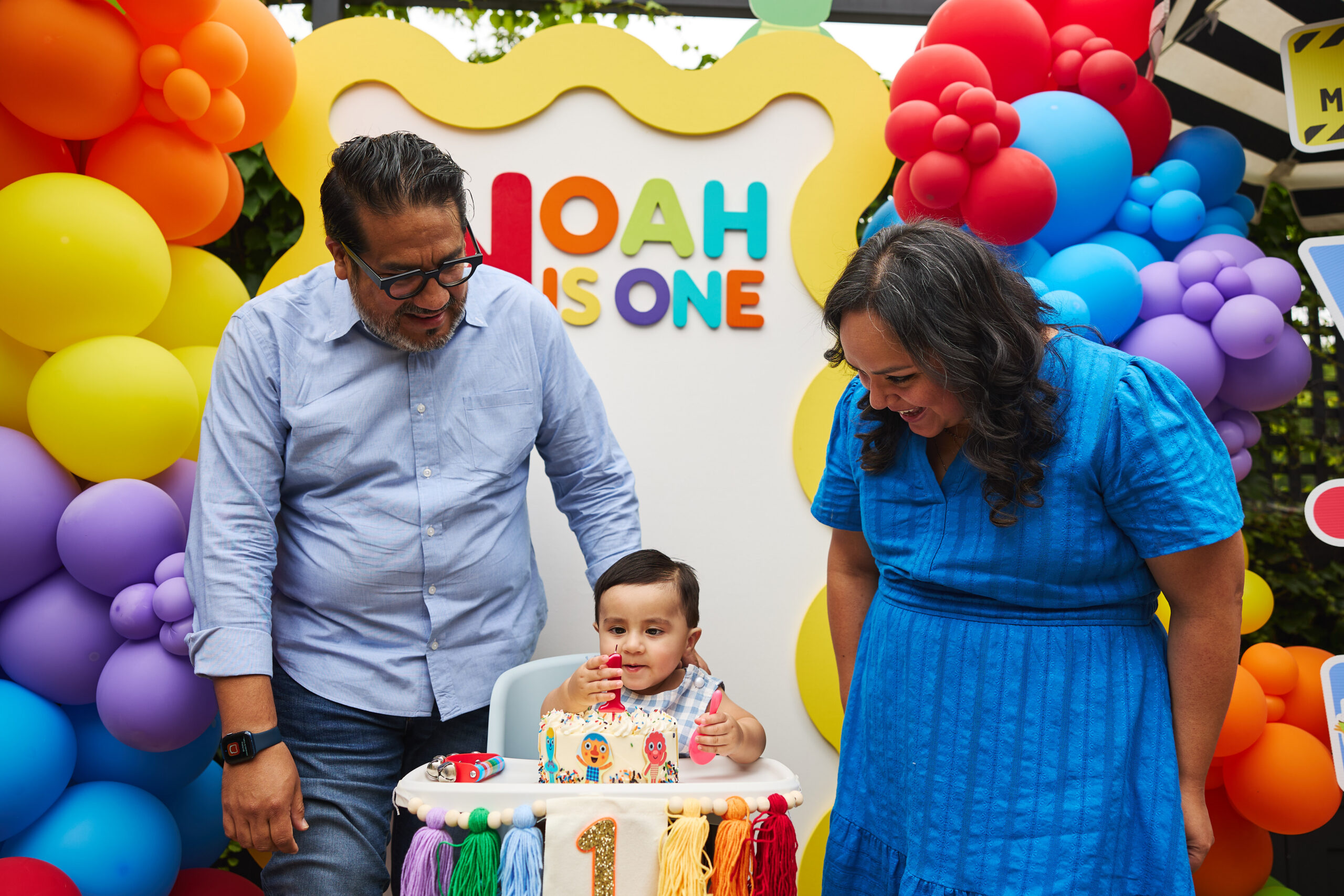 A bright and colorful Super Simple Songs-inspired first birthday setup at The Warbler in Chicago, featuring a primary-colored balloon arch, musical instrument centerpieces, and custom cake decor on a sunlit patio.