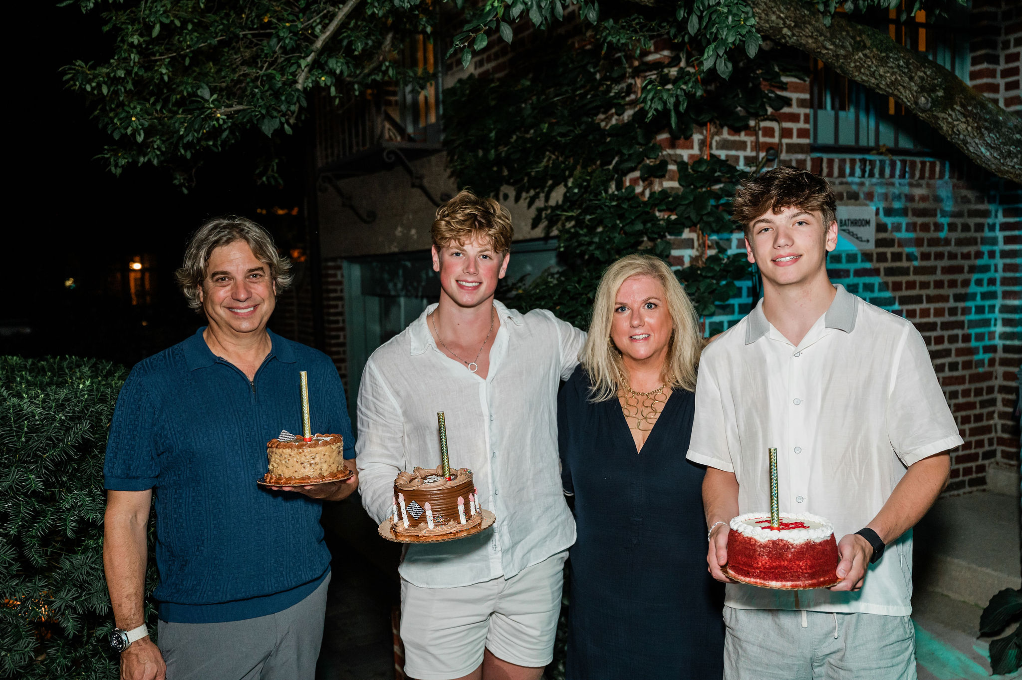 Outdoor evening milestone birthday party setup organized by WE Events in Chicago, featuring a family holding custom birthday cakes outside a historic home.