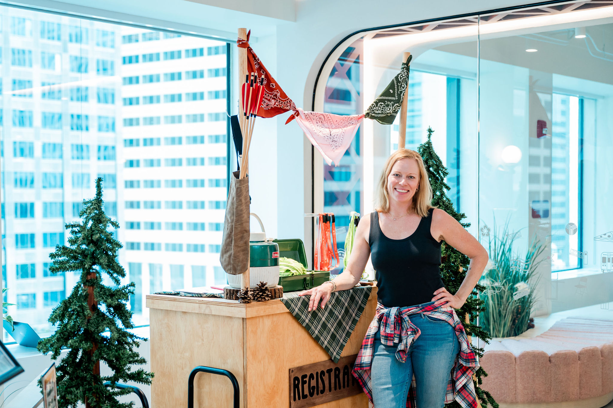 A high-angle view of Pinterest Chicago’s camping-themed Bring Your Kids to Work Day event featuring branded directional trail signs, interactive craft tables, canvas teepees, and green foliage set up inside a corporate office.